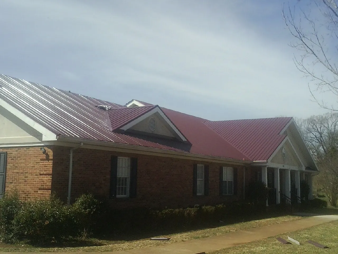 Red metal roof with gabled entries on a long brick building, from a Hail Damage Roof Repair job in Clallam Bay