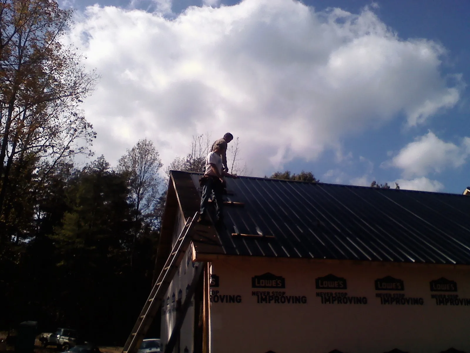 Roofer fastening dark metal panels high against a cloudy sky, from a Roof Inspection job in Clallam Bay