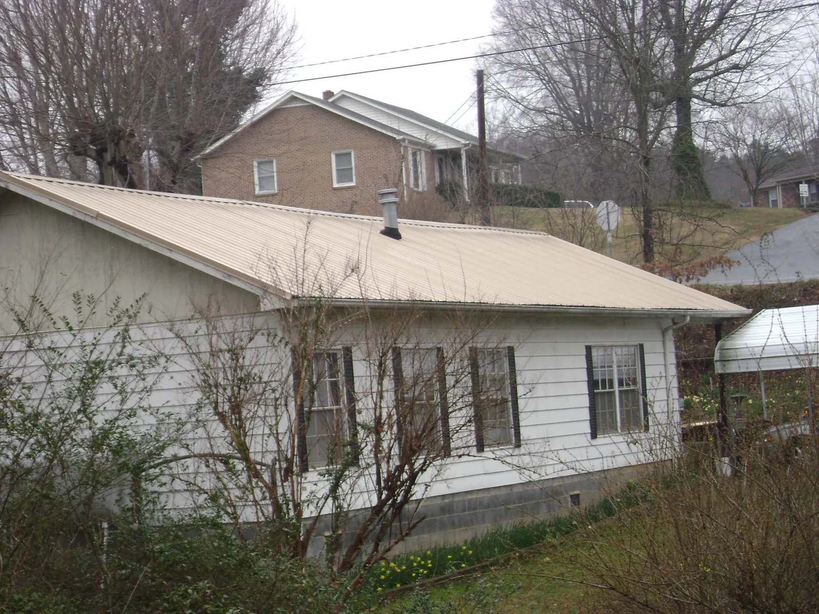 Tan metal roof on a white sided house set into a hillside — Commercial Roofing by Roofing Brothers in Clallam Bay
